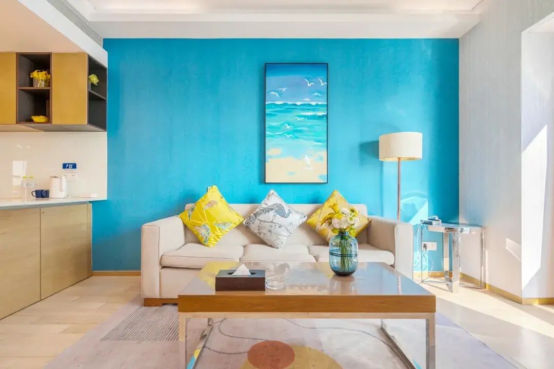 Ein modernes Wohnzimmer mit blauer Akzentwand, einer Couch mit dekorativen Kissen, einem Couchtisch und einem Gemälde von einer Strandansicht.