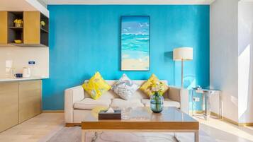 Ein modernes Wohnzimmer mit blauer Akzentwand, einer Couch mit dekorativen Kissen, einem Couchtisch und einem Gemälde von einer Strandansicht.