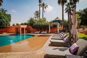A swimming pool with lounge chairs and umbrellas, surrounded by palm trees and greenery. - Palais Wassim Marrakech (Marrakech)