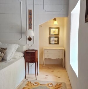 Un dormitorio con cama, mesita de noche y lámpara de pared. Se aprecia un pequeño aparador con cajones.