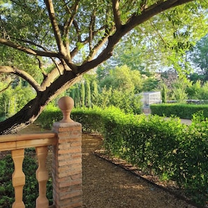 Een tuin met een bakstenen pijler, een houten omheining en diverse beplanting, waaronder bomen en hagen.
