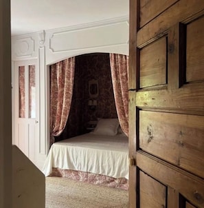 Un dormitorio con cama, puerta de madera y cortinas estampadas.