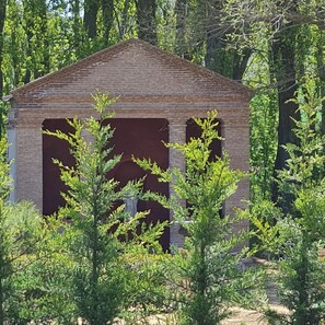 Una construcción de ladrillo con techo triangular, rodeada de abundante follaje verde.