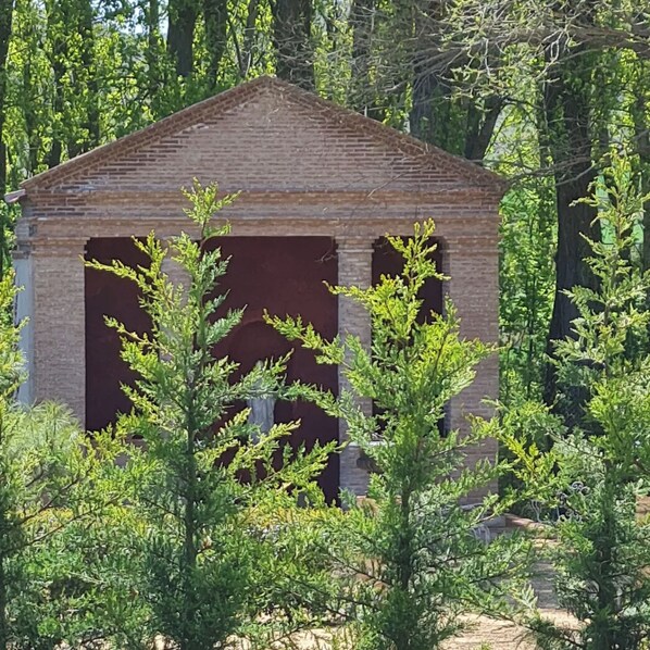 Een gebouw van baksteen met een puntig dak, omgeven door weelderige groene begroeiing.