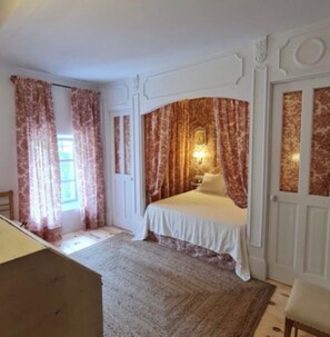 Un dormitorio con cama, cortinas, mesita de noche y lámpara de pared.