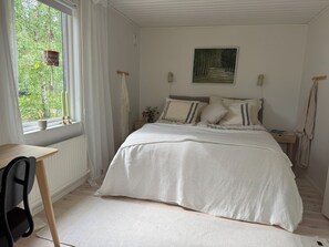 Ein Schlafzimmer mit einem Bett, einem Fenster mit Vorhängen, einem Nachttisch und einem Bild an der Wand.