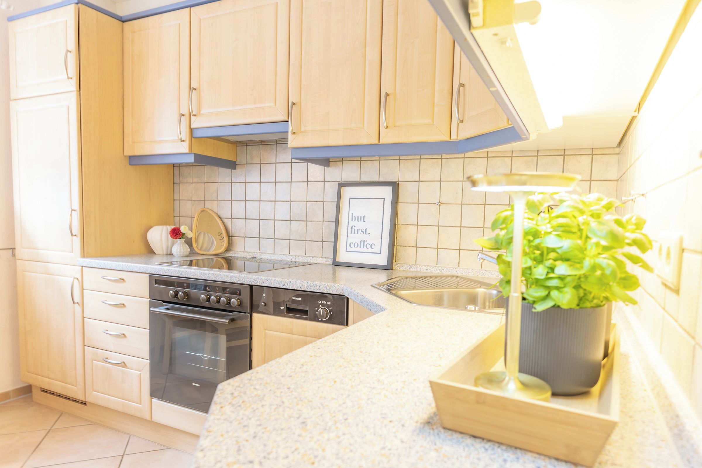 A kitchen with light wooden cabinets, a stainless steel sink, a dishwasher, and a stove.