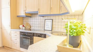 A kitchen with light wooden cabinets, a stainless steel sink, a dishwasher, and a stove.