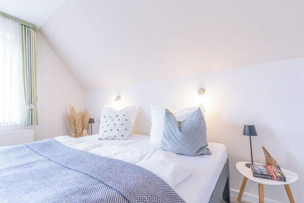 A bedroom with a bed, pillows, a bedside table with a lamp, and a window with curtains. - Your spacious vacation home, Anita, in St. (Sankt Peter-Ording)