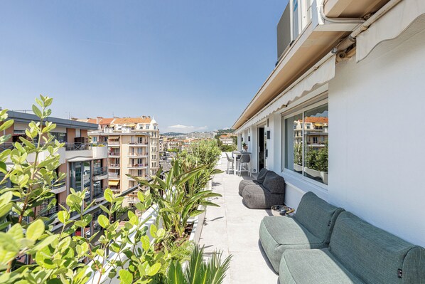 Un balcón con sofá, plantas en macetas y vistas de edificios circundantes.