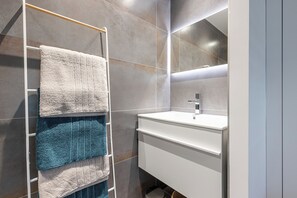 Une salle de bain moderne avec un lavabo blanc, un miroir et un porte-serviettes sur lequel sont disposées plusieurs serviettes.