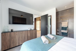 Una habitación de hotel moderna con una cama grande, una mesa consola de madera, un televisor de pantalla plana y un baño con toallero.