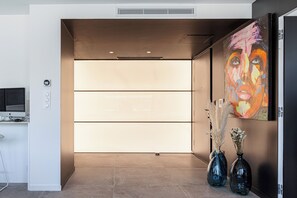 Una moderna zona de recepción con una pantalla digital, un mostrador con un ordenador y dos jarrones con plantas secas.