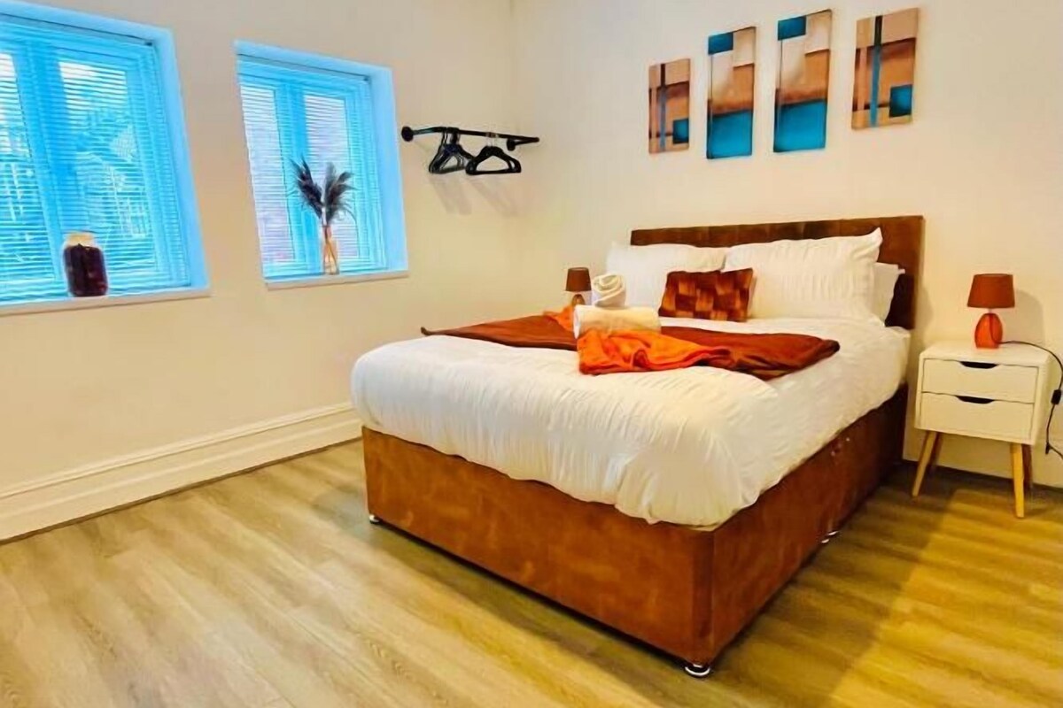Ein Schlafzimmer mit einem großen Bett, einem Nachttisch, einer Lampe und Kunstwerken an der Wand.