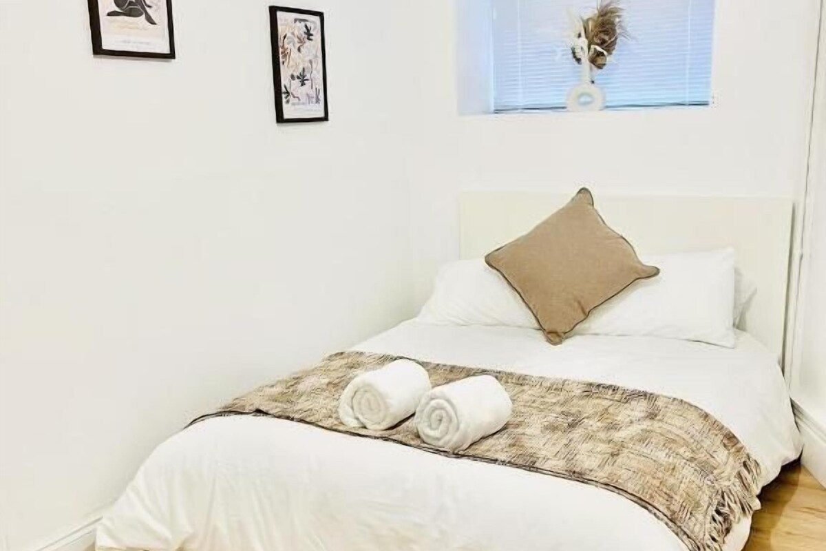 Ein Schlafzimmer mit einem Bett, einem Fenster und zwei gerahmten Bildern an der Wand.