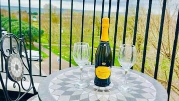 Une table ronde avec une bouteille de vin et deux verres, posée sur un balcon doté d’une rambarde en métal.