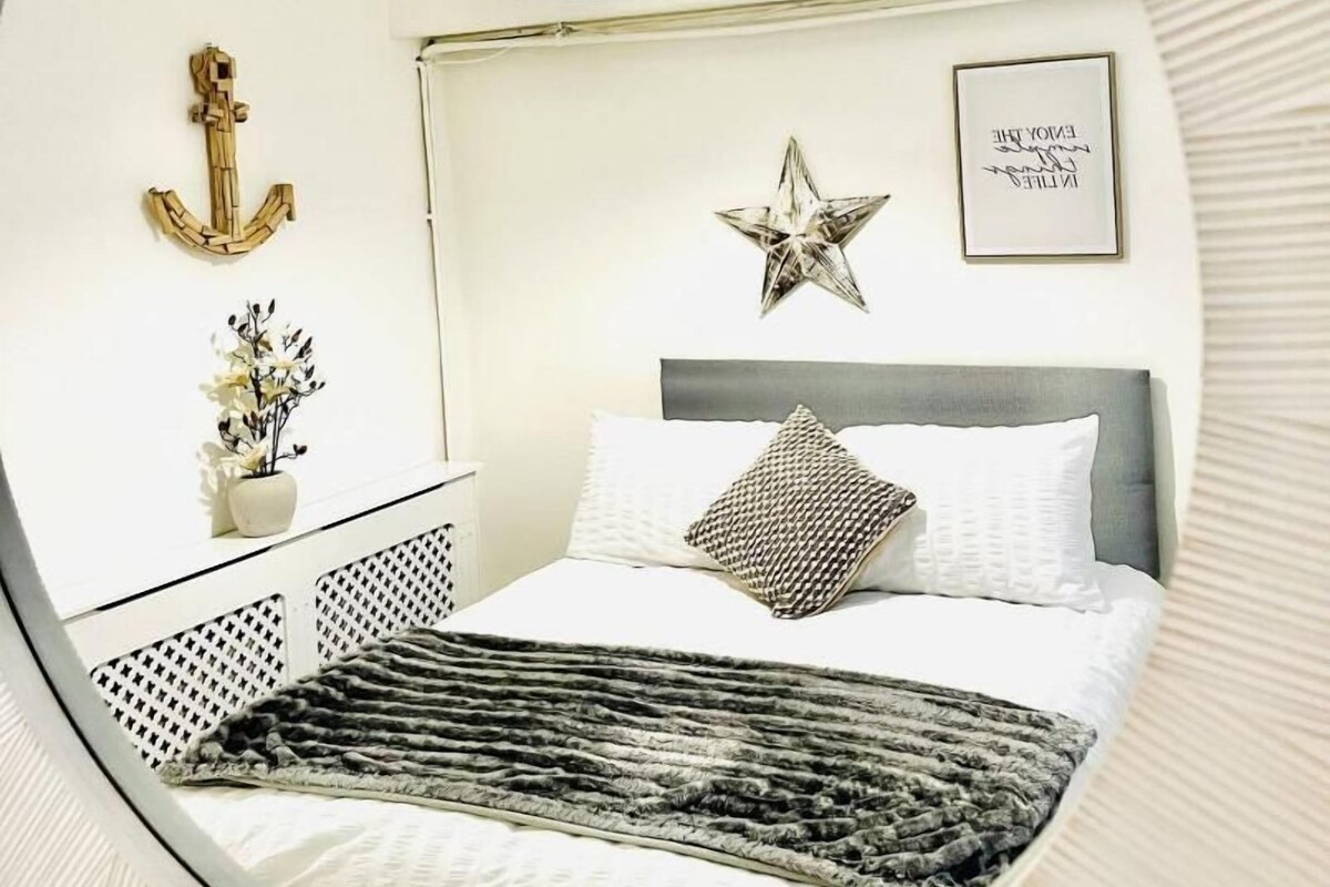 Ein Schlafzimmer mit einem Bett, einem Nachttisch, einer Lampe und Wanddekorationen, darunter ein Anker und ein Stern.