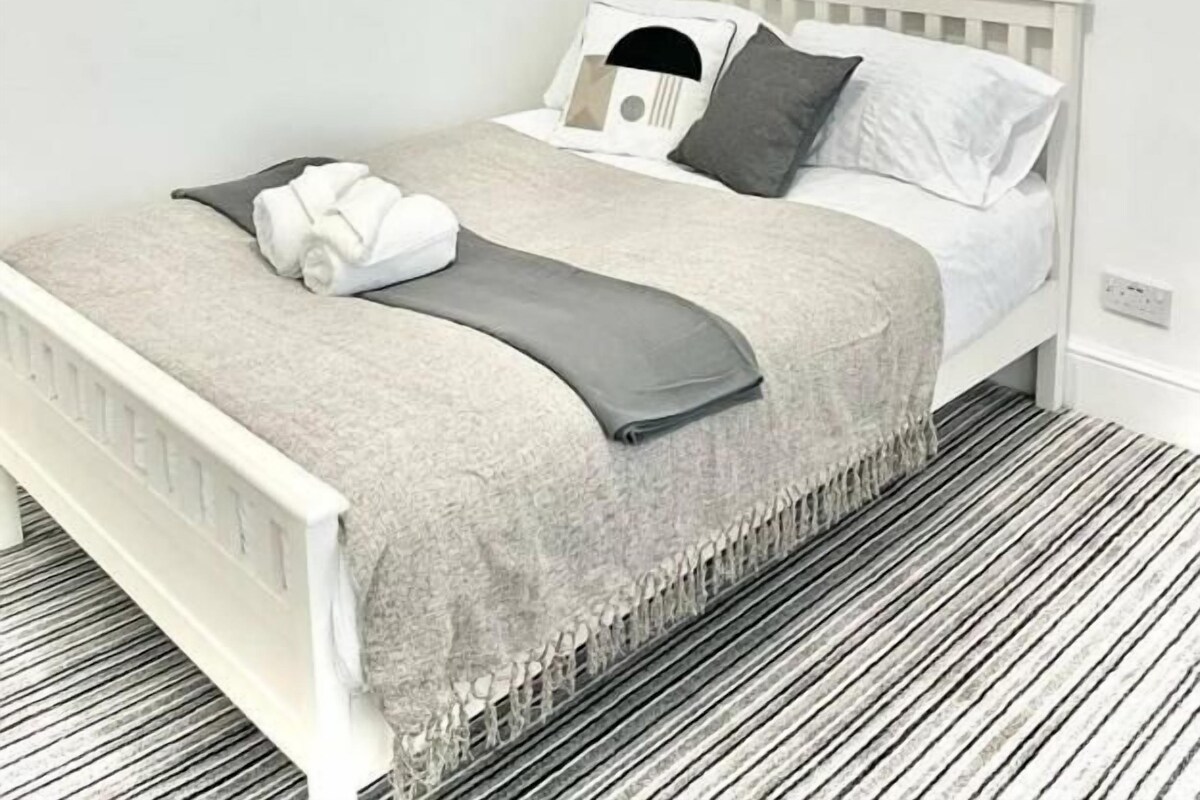 Ein ordentlich bezogenes Bett mit einem weißen Kopfteil, einer grauen Decke und einem grauen Zierkissen.