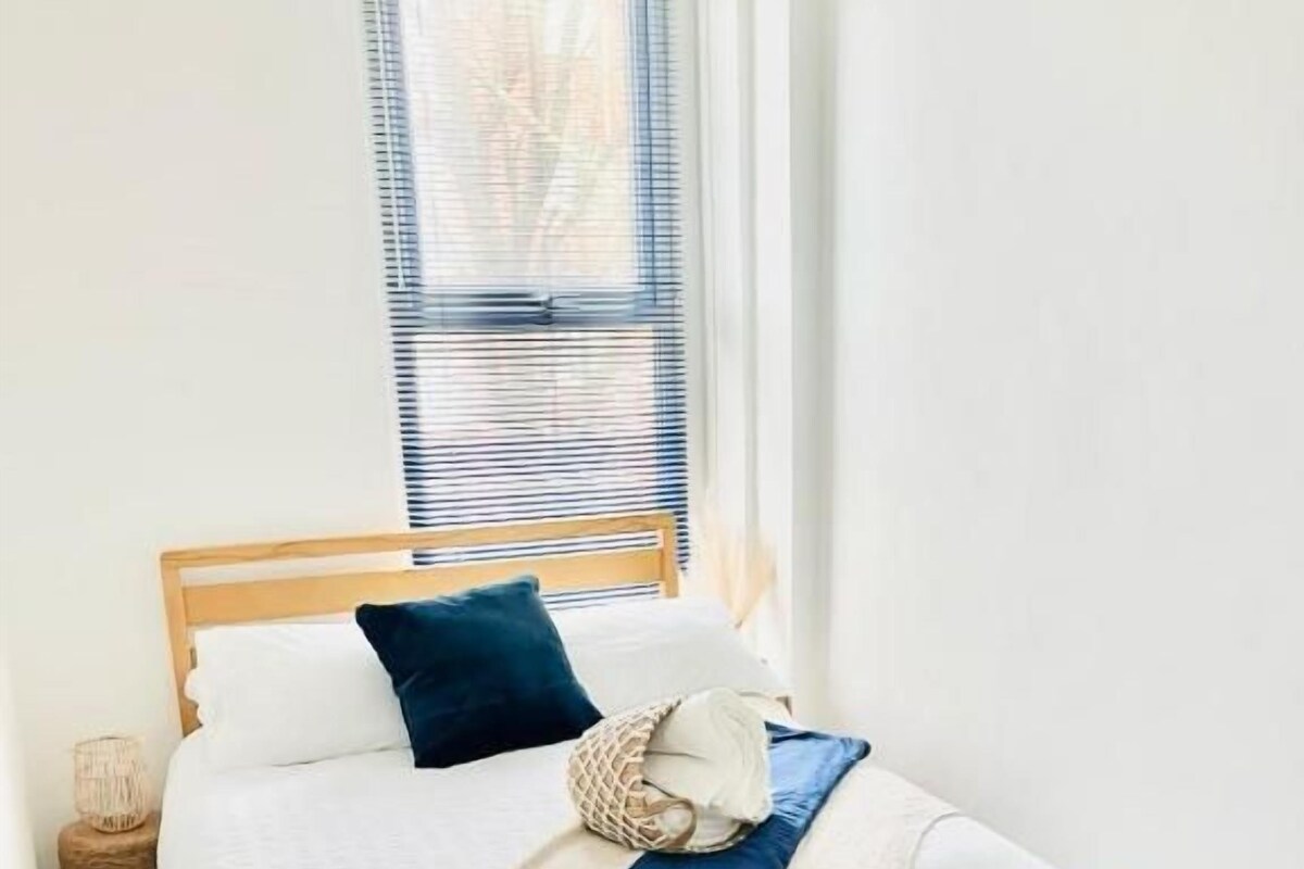 Ein Einzelbett mit Holzrahmen, weißer Bettwäsche und einem blauen Kopfkissen.