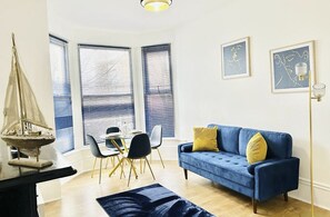 Ein modernes Wohnzimmer mit einem blauen Sofa, einem Esstisch mit Stühlen und Bildern an den Wänden.