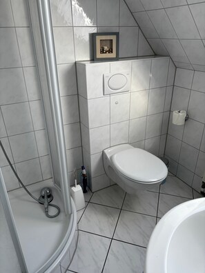 A bathroom with a toilet, shower, and a framed picture on the wall. - Apartment 'Lina' with Wi-Fi (Grömitz)