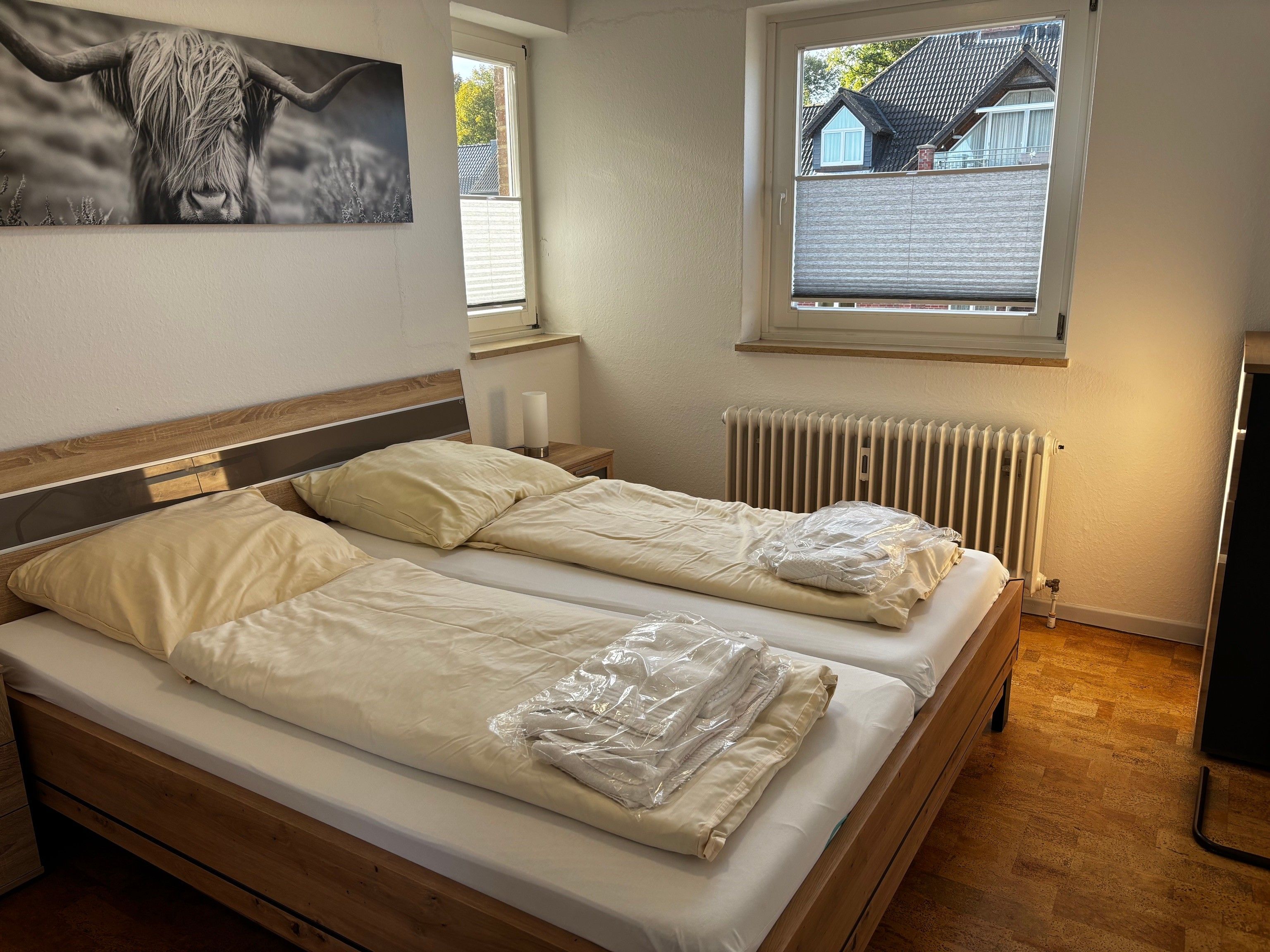 A double bed with a wooden headboard, a bedside table with a lamp, and a window with blinds.