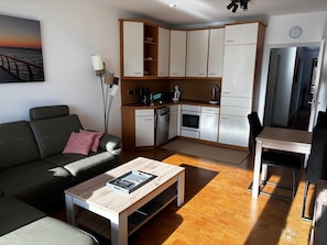 Un espacio habitable compacto con kitchenette, comedor y zona de estar con mesa de centro.