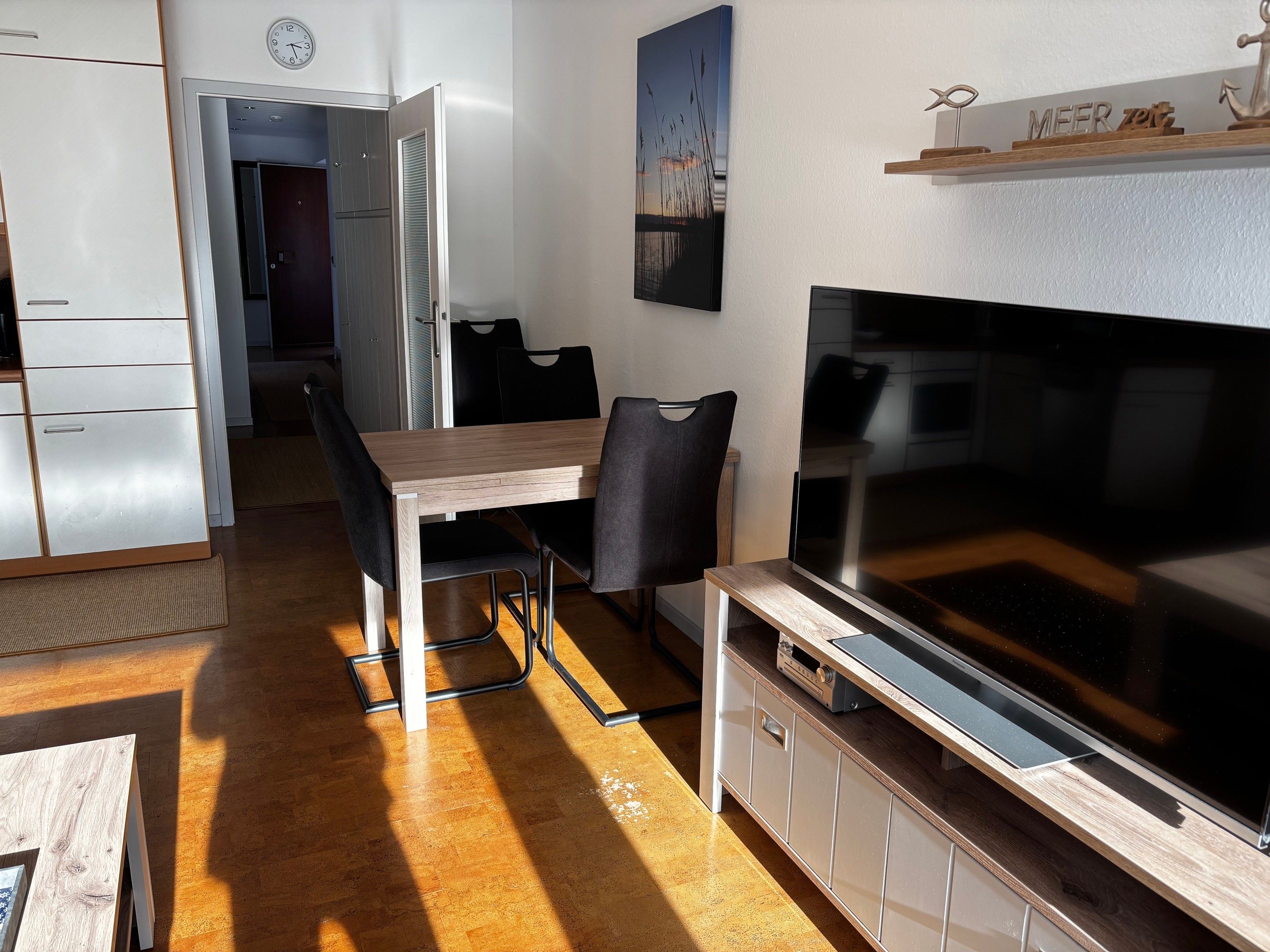 A modern kitchen with a dining area, a large flat-screen TV, and a wooden table.