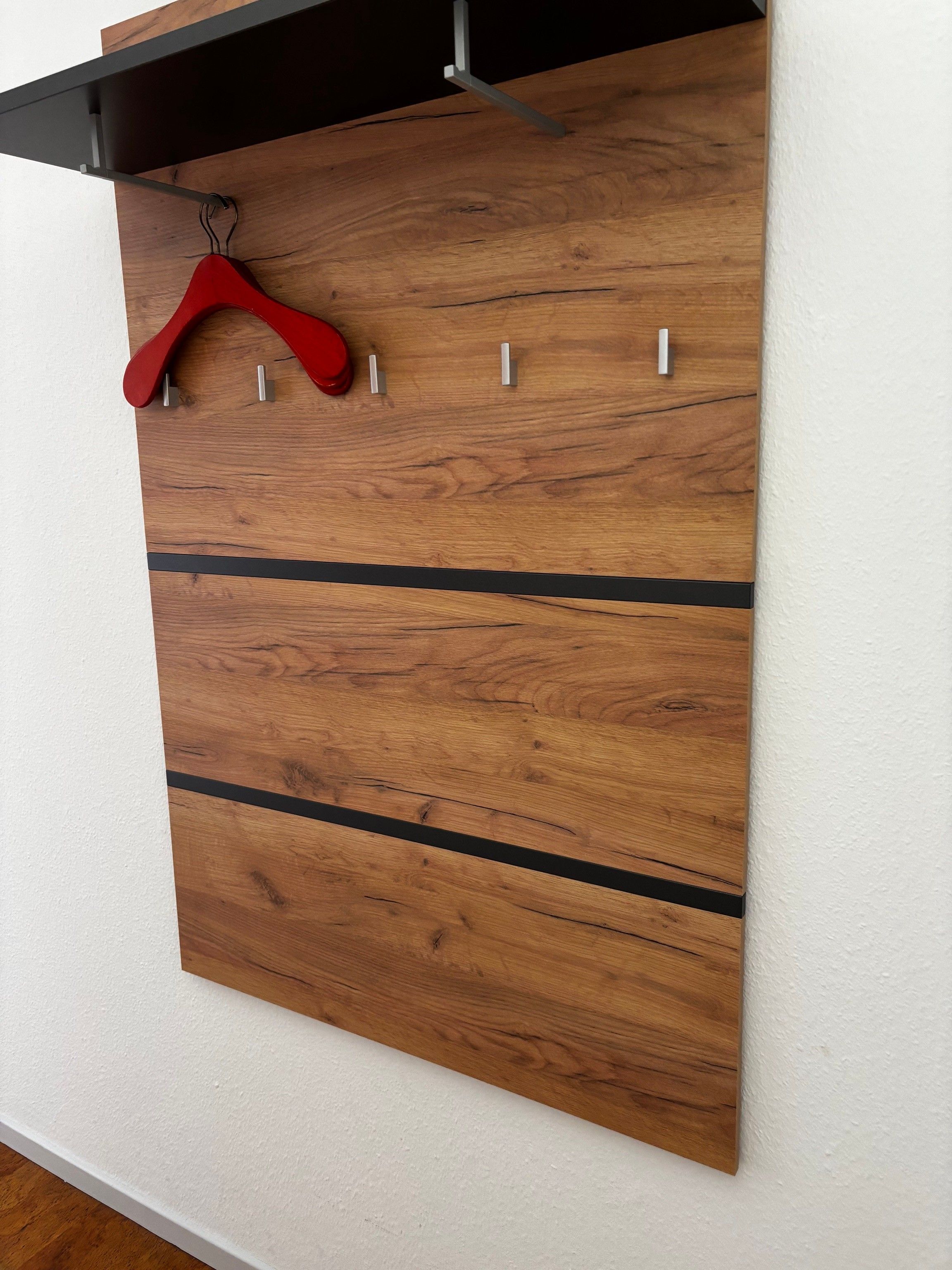 Un panel de madera fijado a la pared con un perchero rojo y ganchos metálicos.