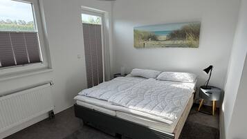 Ein Schlafzimmer mit einem Bett, einem Heizkörper, einem Fenster mit Jalousien, einem Bild an der Wand und einer Nachttischlampe.