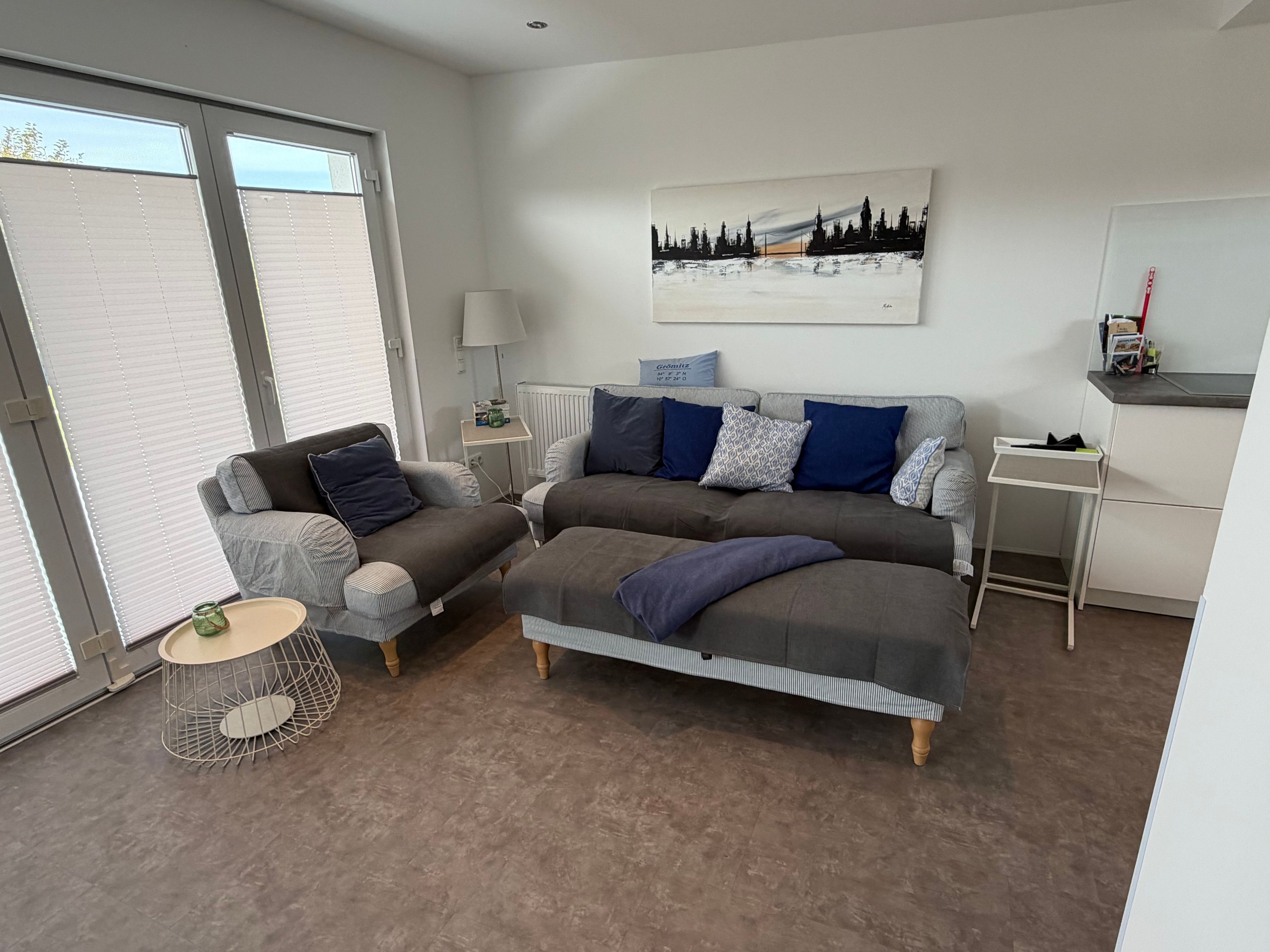 Una sala de estar moderna con un sofá, un sillón y una mesa de centro. Hay un cuadro en la pared, una lámpara y un radiador.