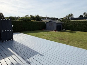 A deck with a wooden floor, a small shed, and a hedge in a residential setting.