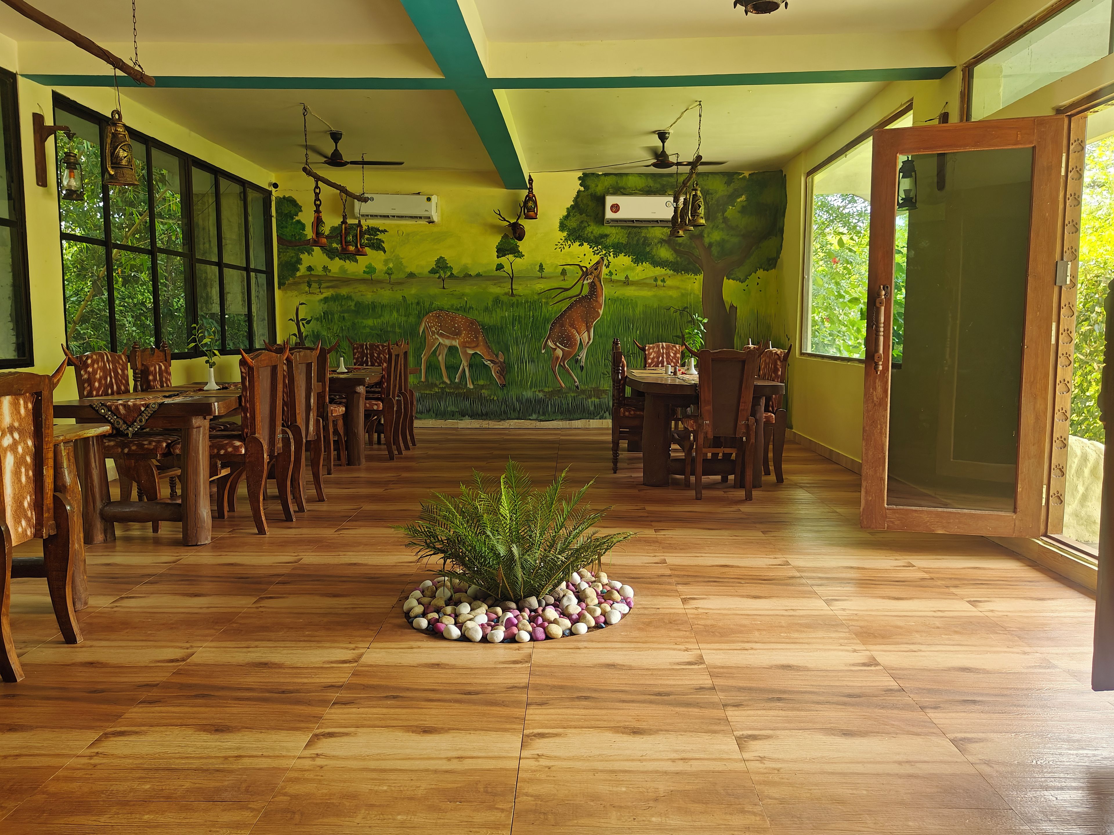 Un comedor con piso de madera, mesas, sillas y un mural de ciervos en la pared.
