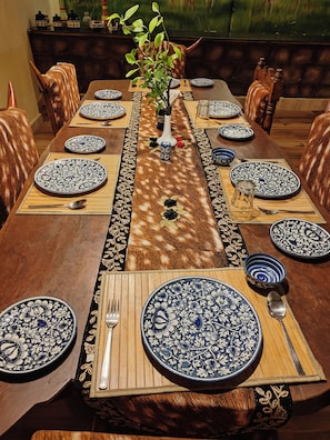 Una mesa de comedor dispuesta con platos de diseño azul y blanco, un florero con una planta y un camino de mesa de madera.
