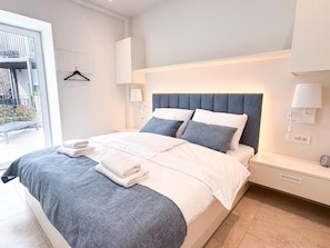 Ein modernes Schlafzimmer mit einem großen Bett, Nachttischlampen und Blick ins Freie.
