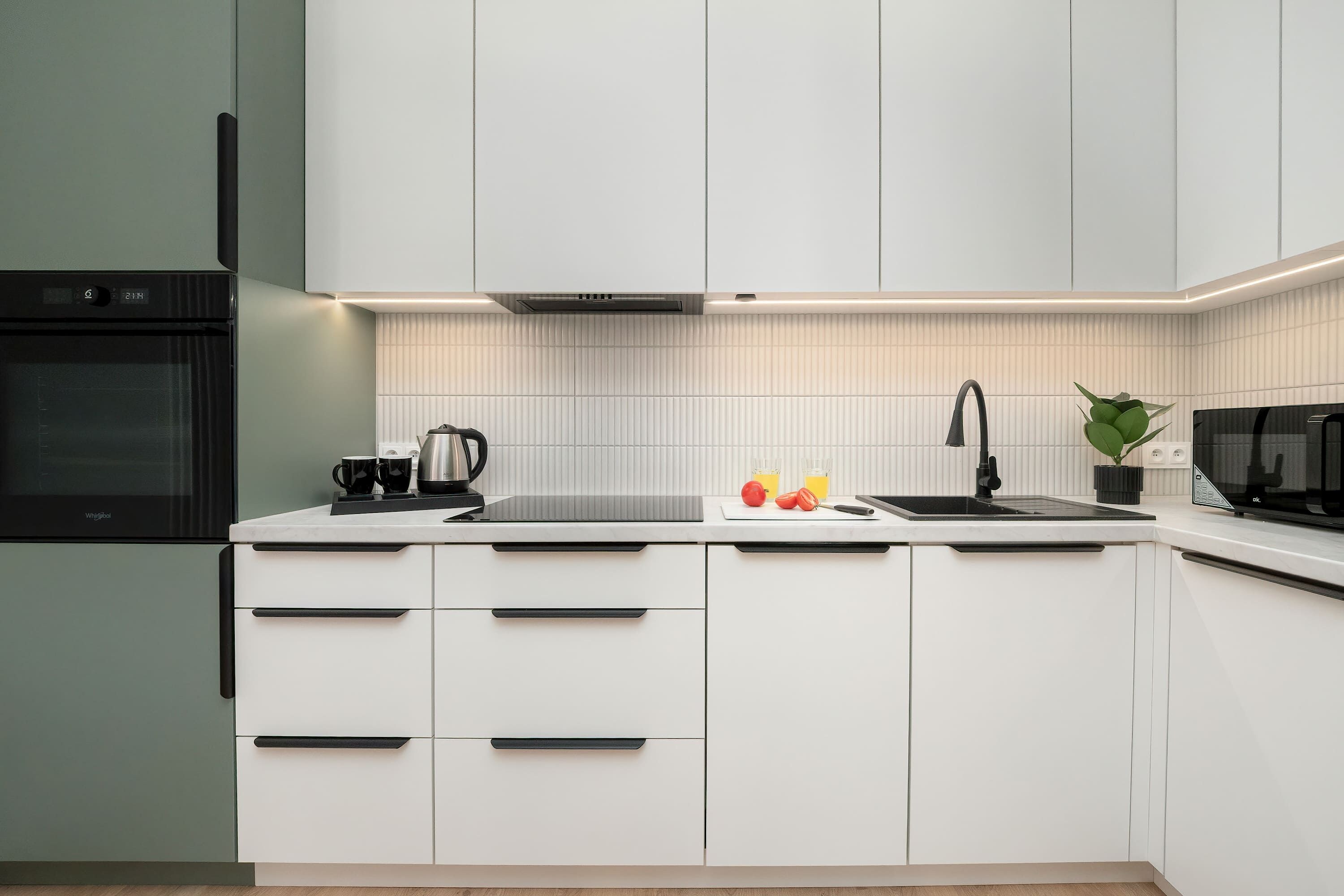 Eine moderne Küche mit weißen Schränken, einem eingebauten Backofen, einer Mikrowelle und einem Spülbecken.