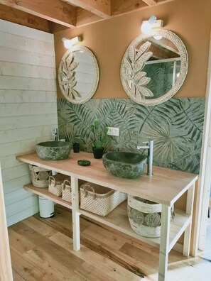 A bathroom with a wooden vanity, two round mirrors, a green textured wall, and wicker baskets.