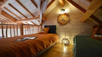 Une chambre avec un plafond en pente, un lit recouvert d’une couverture orange, une table de chevet avec une lampe et un luminaire fixé au mur.