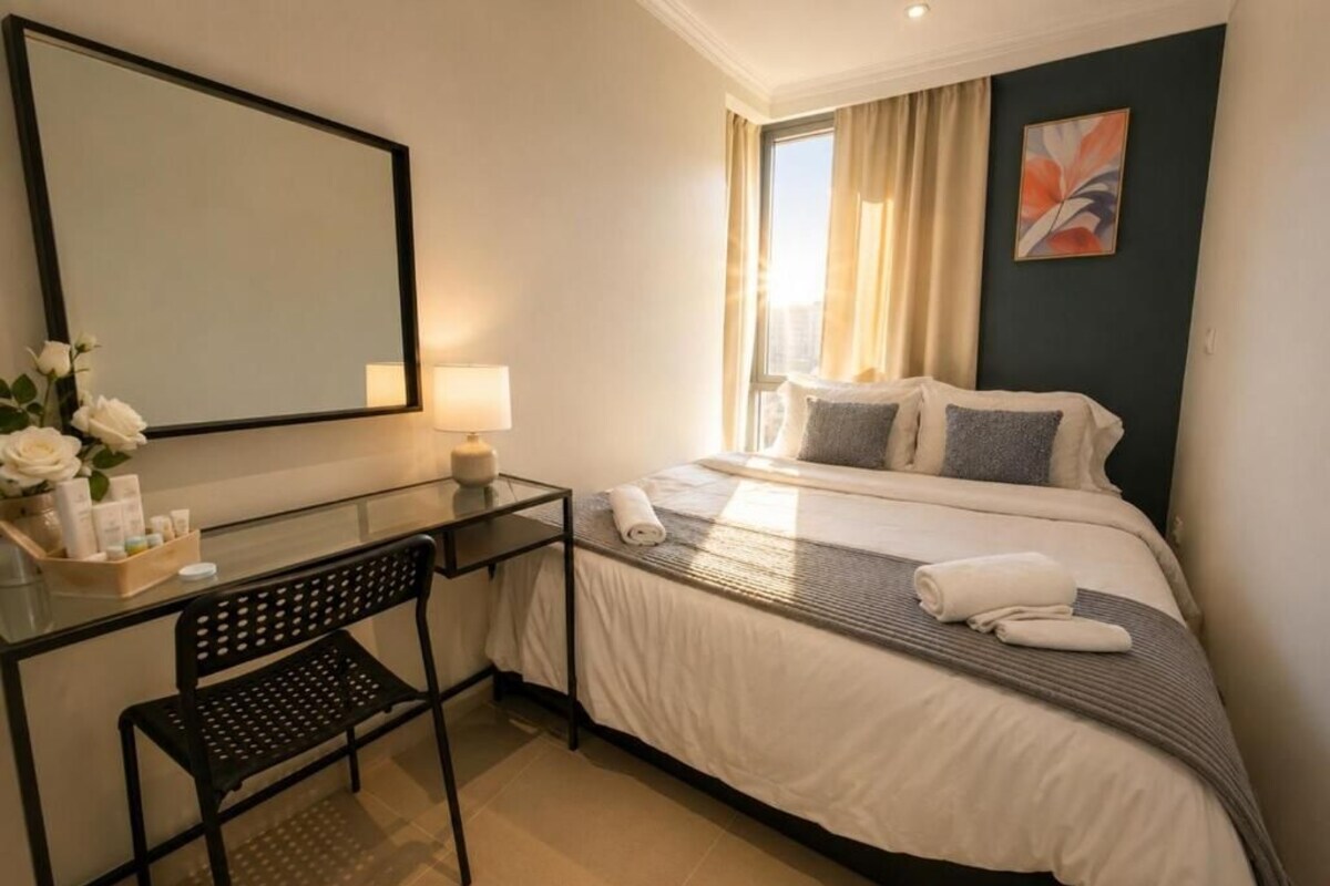 Habitación de hotel con cama, escritorio con silla, espejo y ventana con cortinas.
