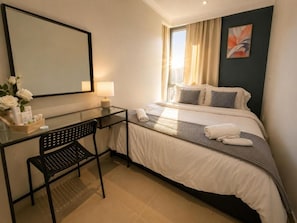 Habitación de hotel con cama, escritorio con silla, espejo y ventana con cortinas.