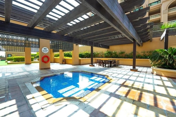 Un área de piscina con suelo de baldosas, una piscina y mobiliario exterior.