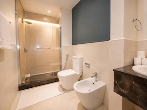 Un baño moderno con ducha envuelta en vidrio, inodoro, bidé y lavamanos con encimera de mármol.