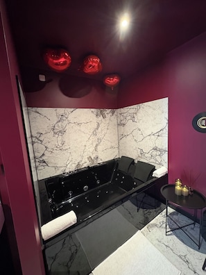 Un baño moderno con una bañera negra, pared de mármol y una pequeña mesa con velas.
