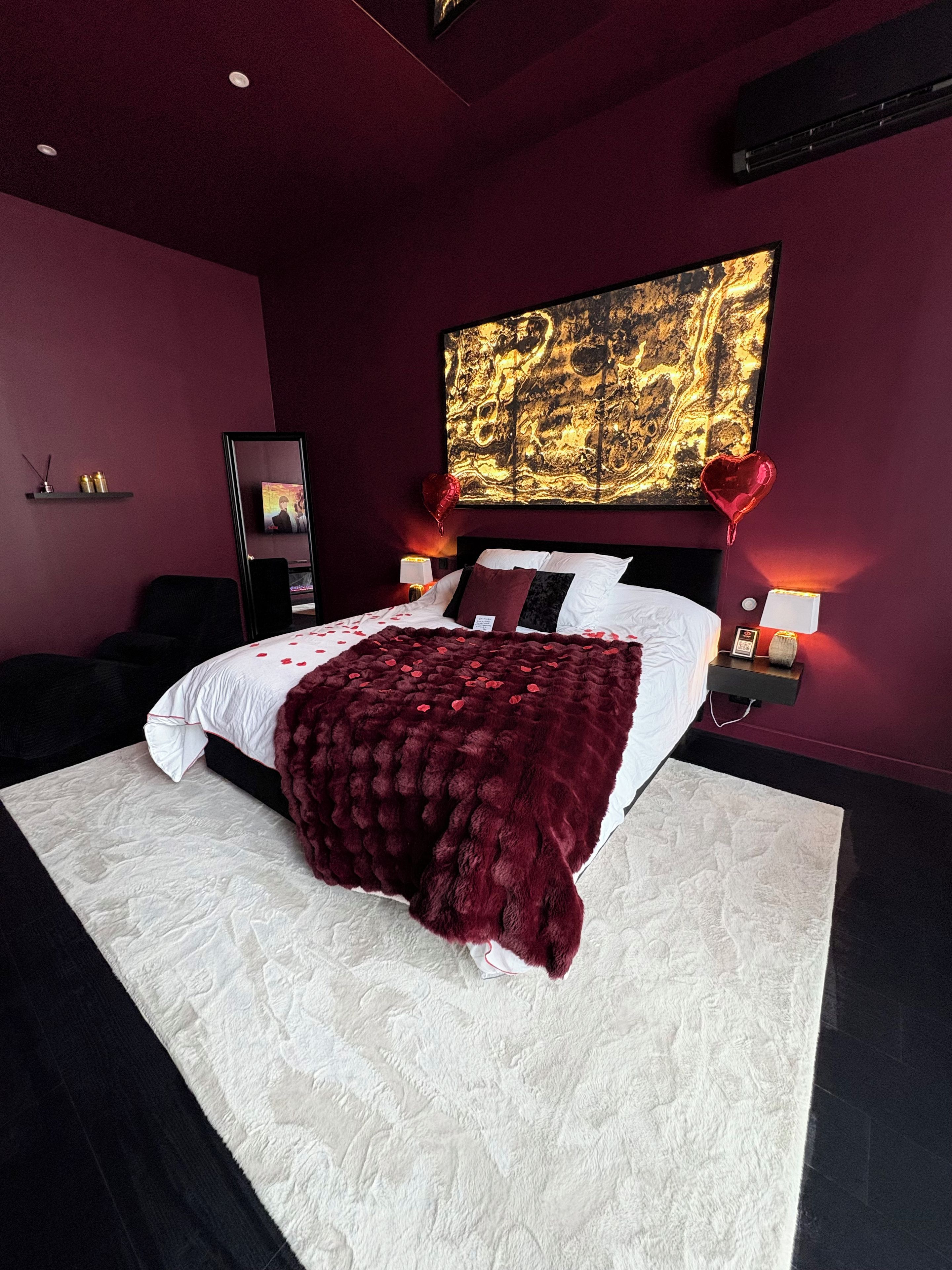 Une chambre moderne avec un grand lit, un ballon rouge en forme de cœur et un grand tableau abstrait accroché au mur.