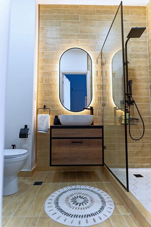 Une salle de bain moderne avec un meuble-lavabo en bois, un miroir rond, un lavabo blanc et une cabine de douche en verre.