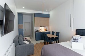 Une chambre d’hôtel moderne équipée d’un canapé, d’un lit, d’une table à manger avec des chaises, d’une kitchenette et d’un téléviseur fixé au mur.