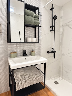 Un baño con lavamanos blanco, un espejo, toallero y ducha.