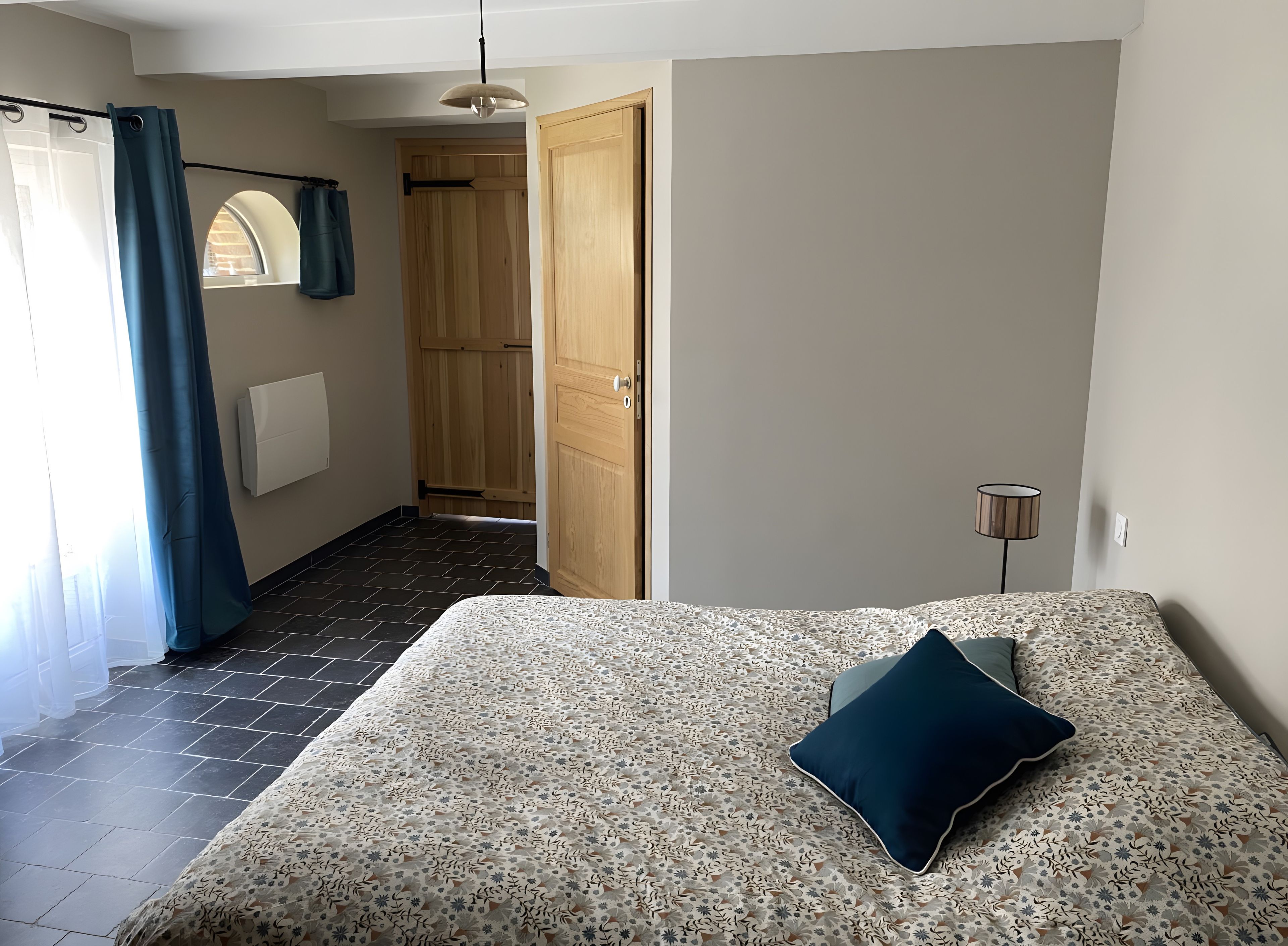 Een slaapkamer met een bed, een nachtkastje, een lamp en uitzicht op een gang.