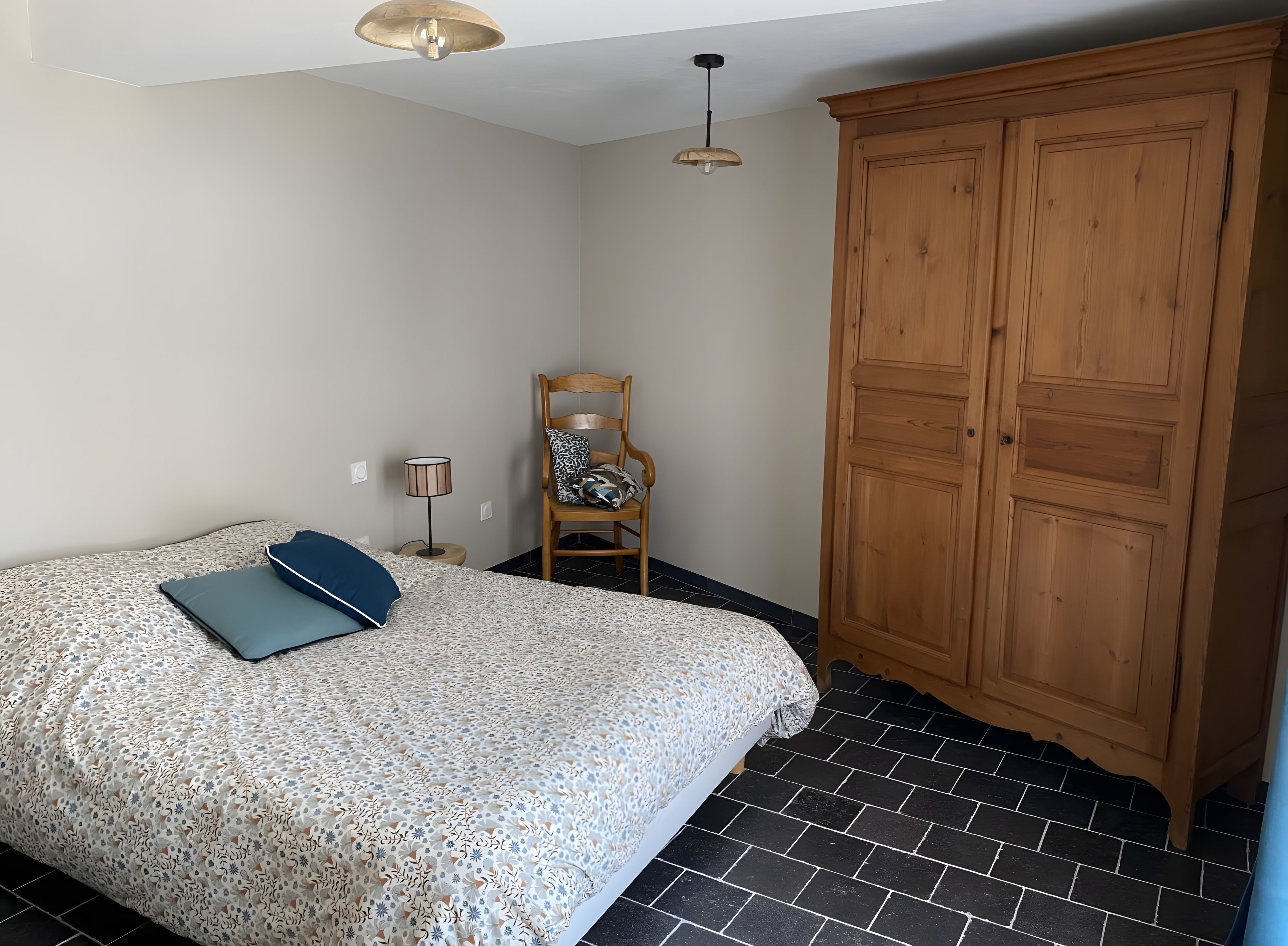 Ein Schlafzimmer mit einem Bett, einem Holzschrank, einem Stuhl und einer Lampe.