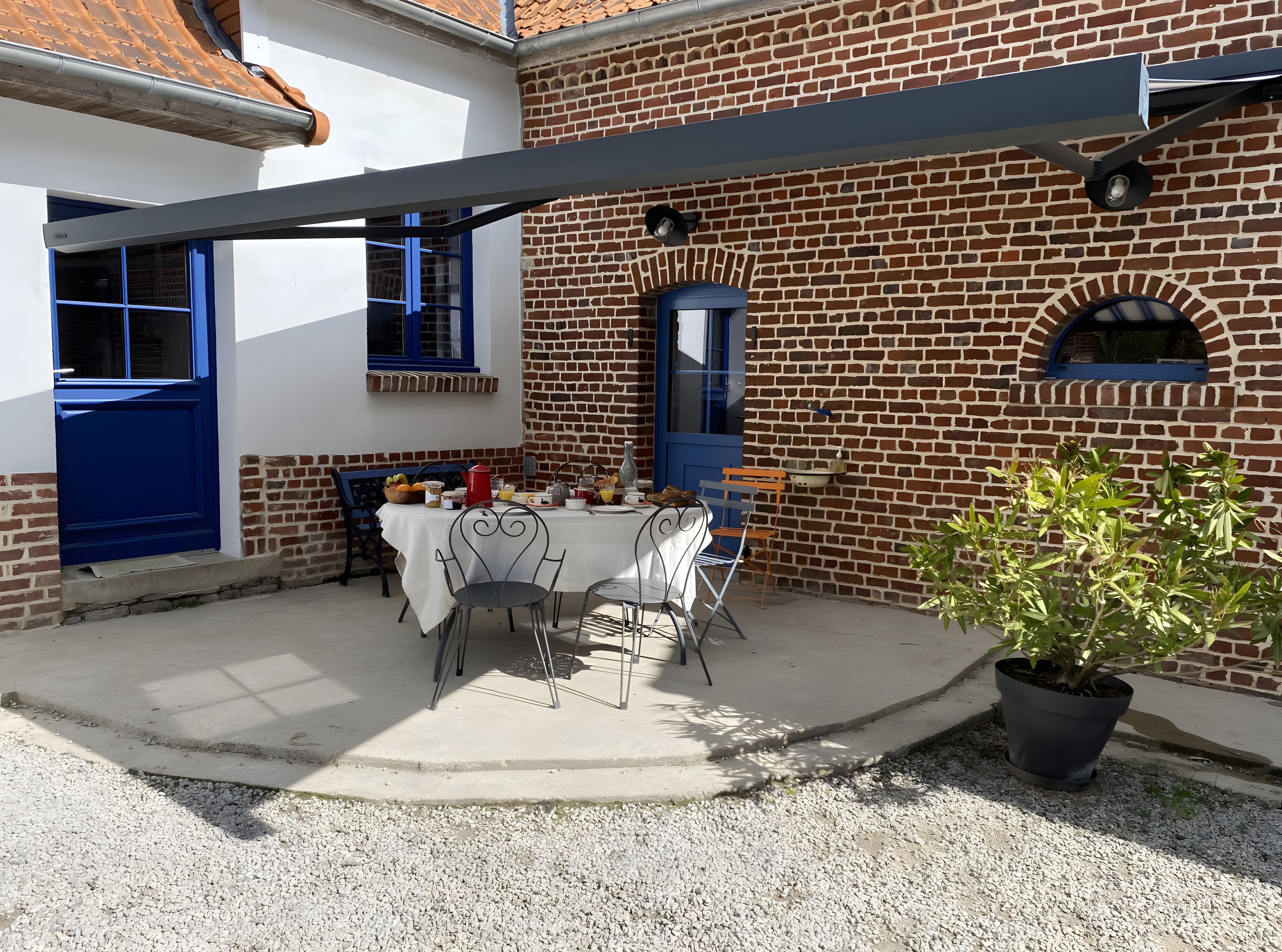Un espace patio avec une table dressée pour les repas, une plante en pot et un mur de briques agrémenté de fenêtres.